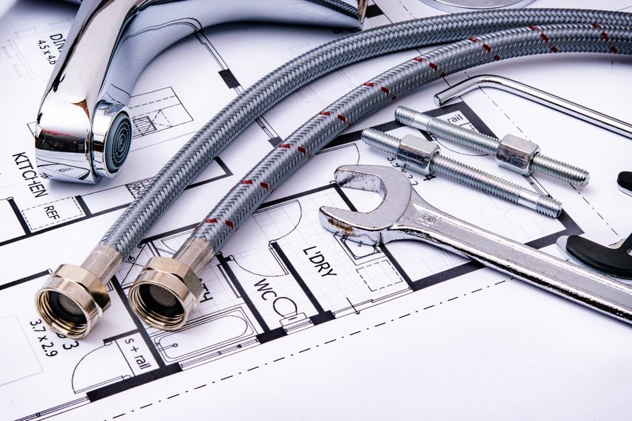 Plumbing fittings and tools laid over house blueprints